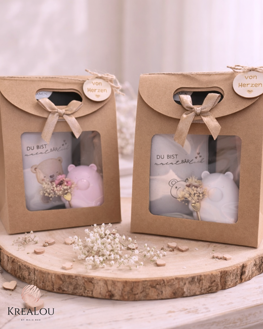Geschenkset in Kraftkarton mit Sichtfenster, Schleife & Holzanhänger, darin ein kleiner PLA-Bär (weiß oder rosa) mit Mini-Blumenstrauß & Tütchen Blumensamen.